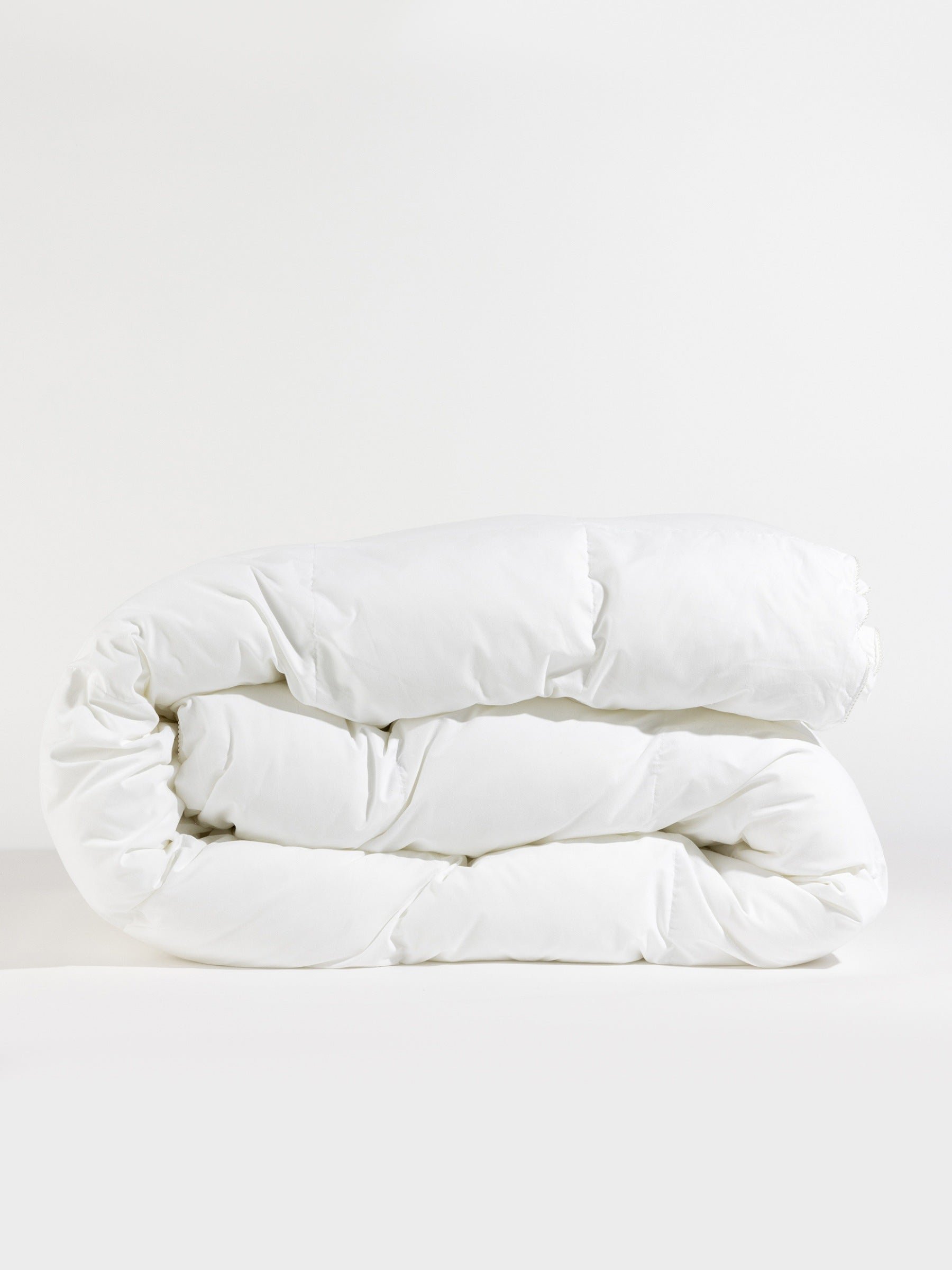 A neatly folded Down Alternative Comforter by Cozy Earth is placed against a plain background. The quilted texture is visible, highlighting its fluffy and soft appearance. |Filling:Standard