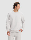 A man wears the Cozy Earth Men's Dylan Crewneck and matching pants, standing against a light background with one hand in his pocket, smiling and looking to his left.|Color:Dew