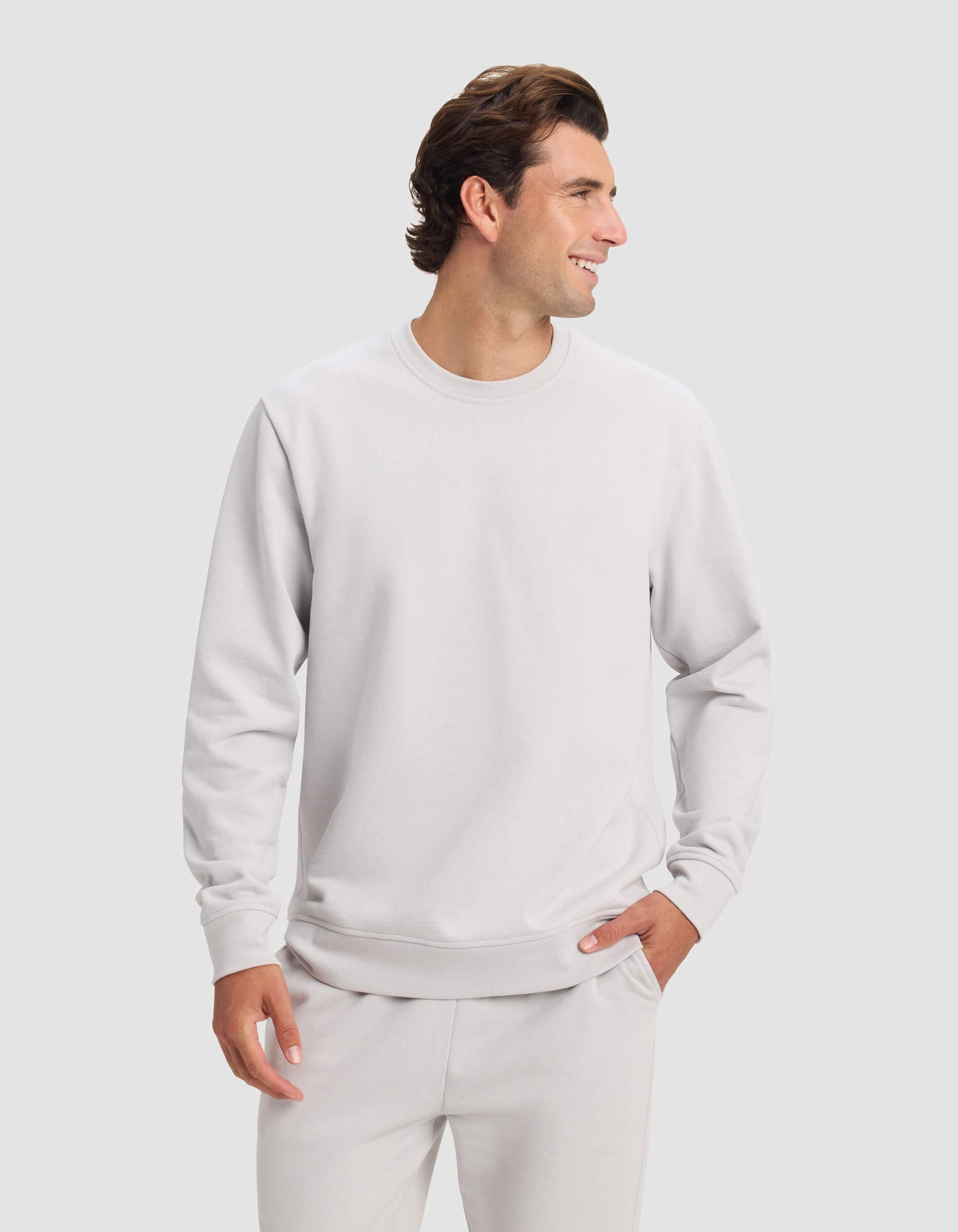 A man wears the Cozy Earth Men's Dylan Crewneck with matching sweatpants, smiling and looking to the side against a plain light background.