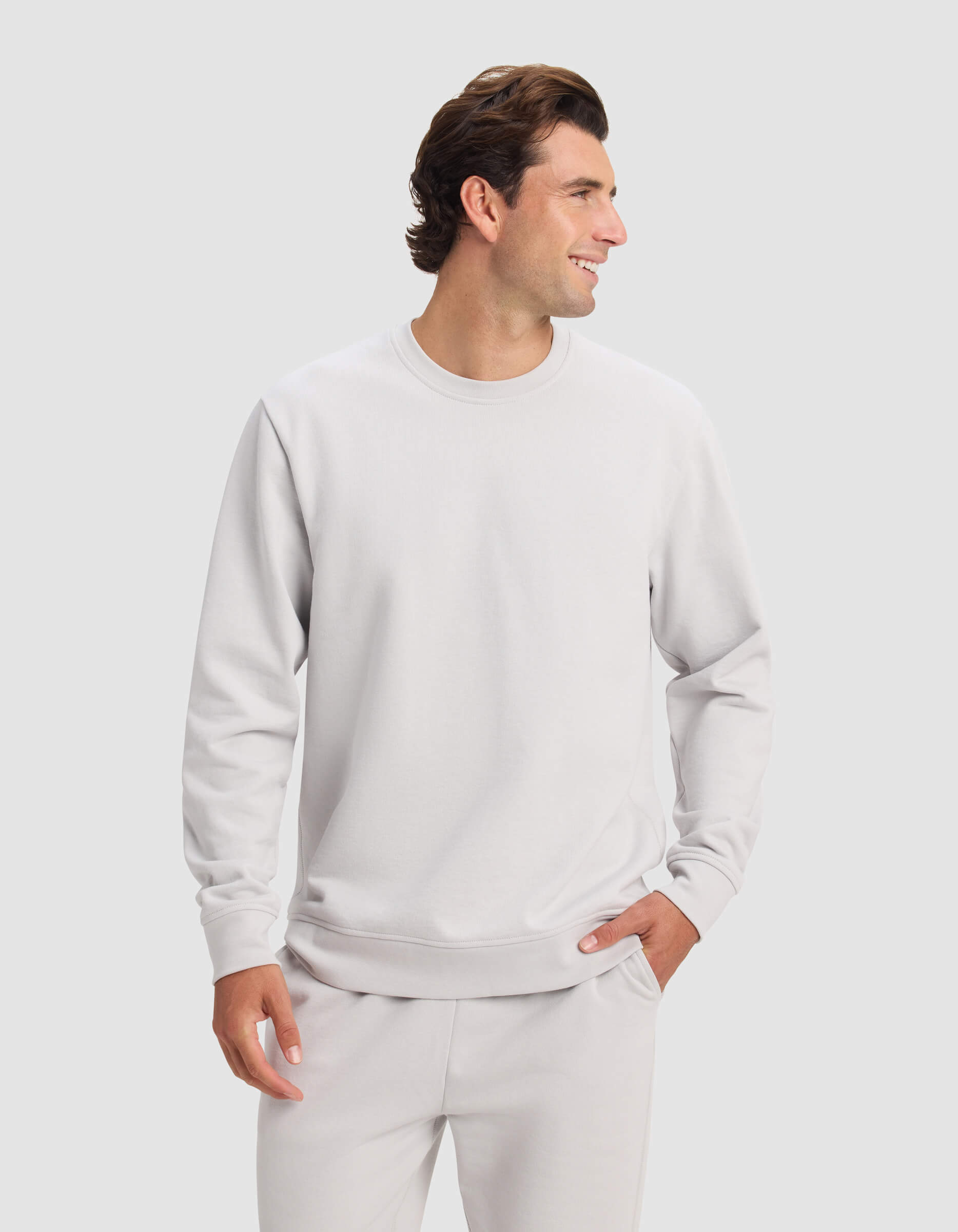 A man wears the Cozy Earth Men's Dylan Crewneck with matching sweatpants, smiling and looking to the side against a plain light background.|Color:Dew