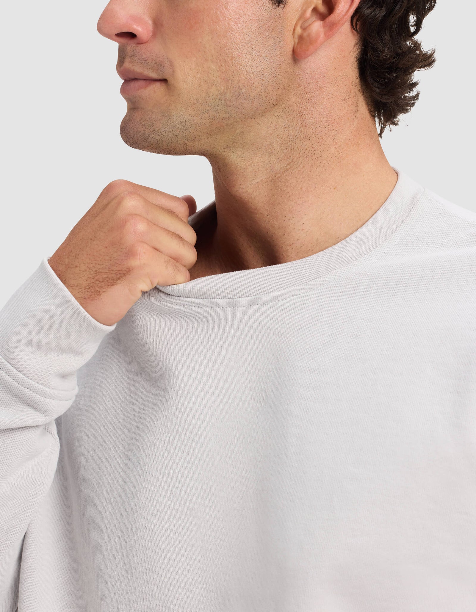 A man wears the Cozy Earth Men's Dylan Crewneck, gently pulling the collar away from his neck with his right hand. Only his lower face and upper torso appear against a plain background.