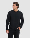 A man models the Cozy Earth Men's Dylan Crewneck and matching black pants, standing against a light gray background with one hand in his pocket and gazing to his right.|Color:Jet Black