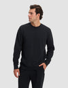 A man wearing the Cozy Earth Men's Dylan Crewneck in black and matching black pants stands against a light gray background, looking to his left with one hand in his pocket.|Color:Jet Black
