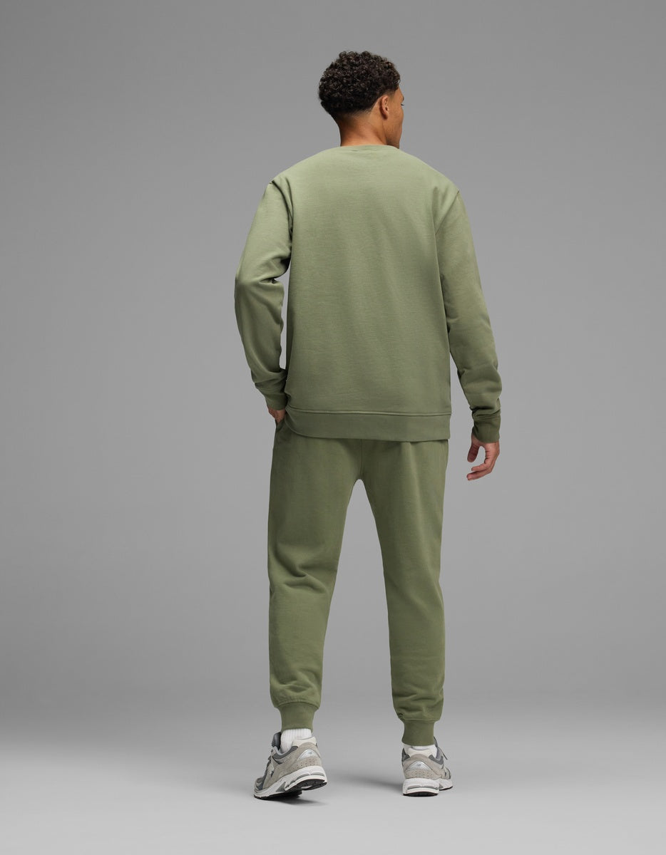 A man seen from behind wearing an olive green Men’s Dylan Crewneck & Jogger Set with cuffed ankles and gray athletic shoes.