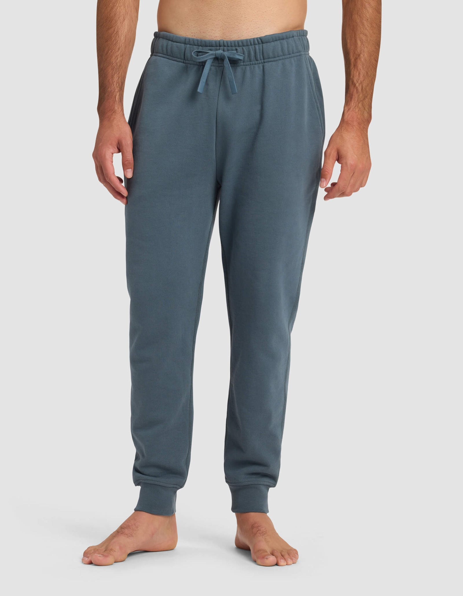 A barefoot man models the Cozy Earth Men's Dylan Jogger in blue, standing against a plain white background with his hands relaxed at his sides.