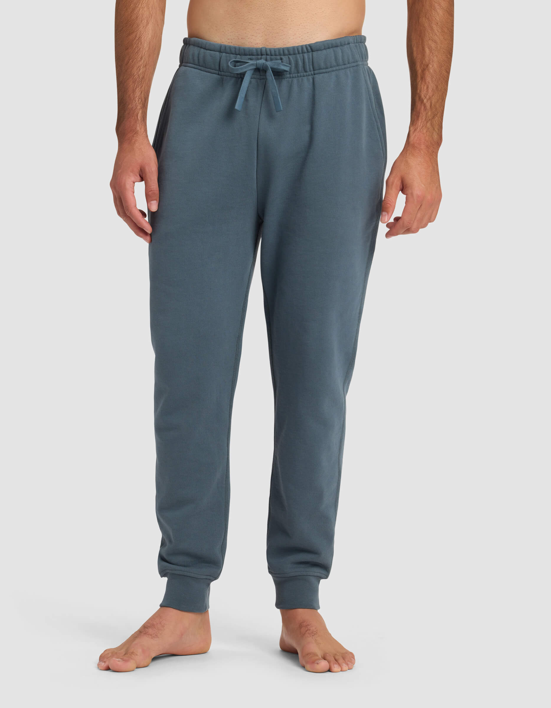 A barefoot man models the Cozy Earth Men's Dylan Jogger in blue, standing against a plain white background with his hands relaxed at his sides.|Color:Dawn