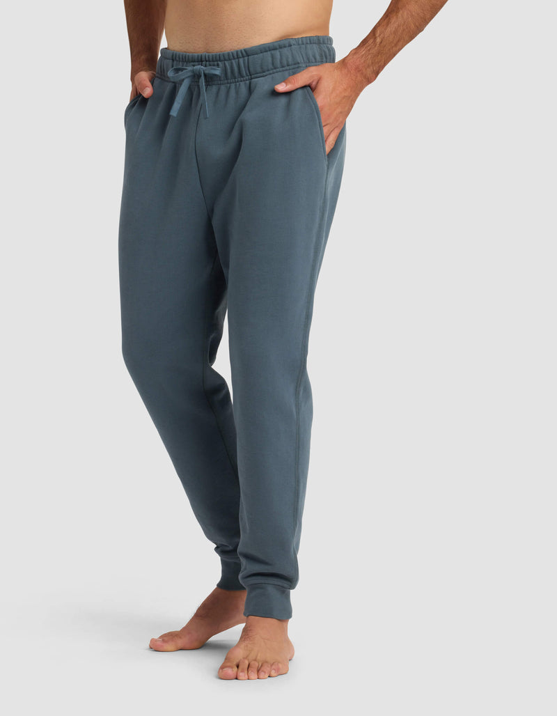A person stands barefoot with hands in pockets, wearing Cozy Earth's Men's Dylan Jogger, against a plain light background.