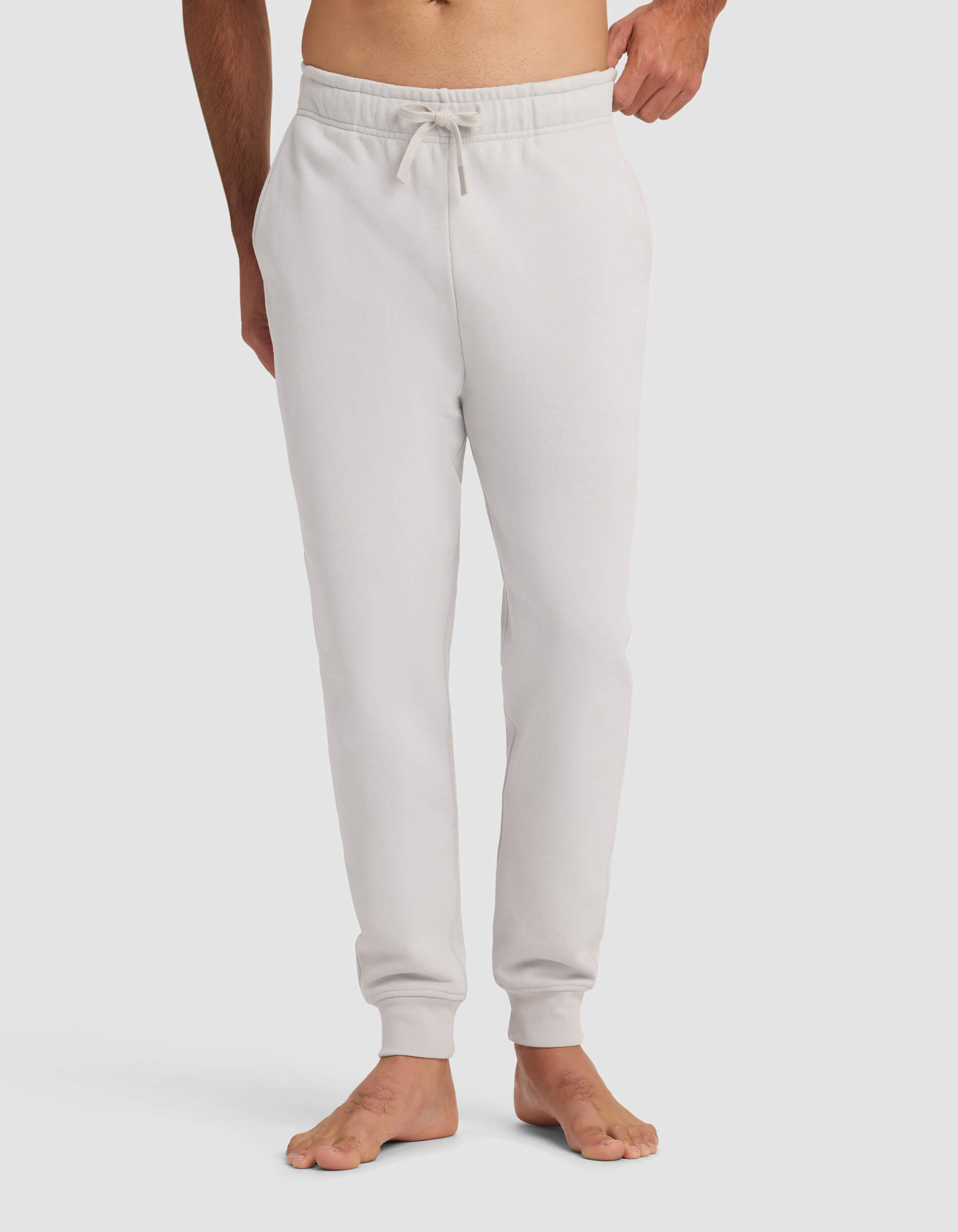 A barefoot person wears Cozy Earth's Men's Dylan Jogger in light gray, featuring an elastic waistband and drawstring, standing against a plain white background.