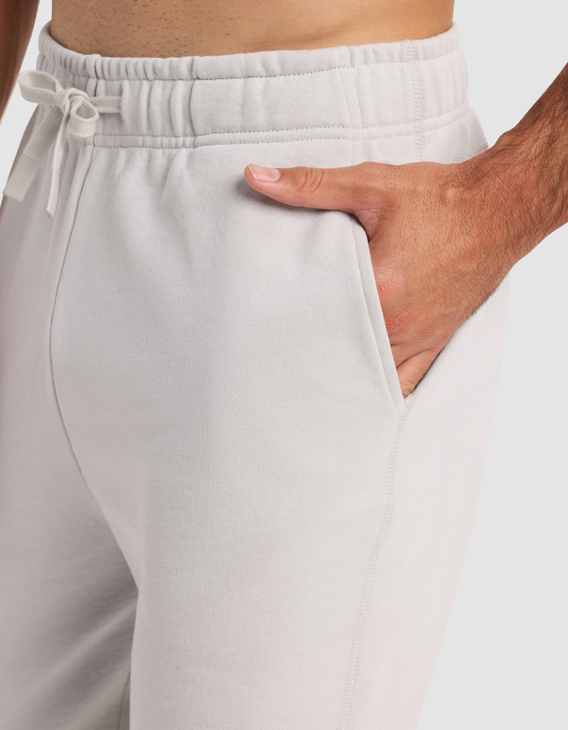 A man models the Cozy Earth Men's Dylan Jogger in light gray, with one hand in the pocket, highlighting the drawstring waistband and side seam detail.