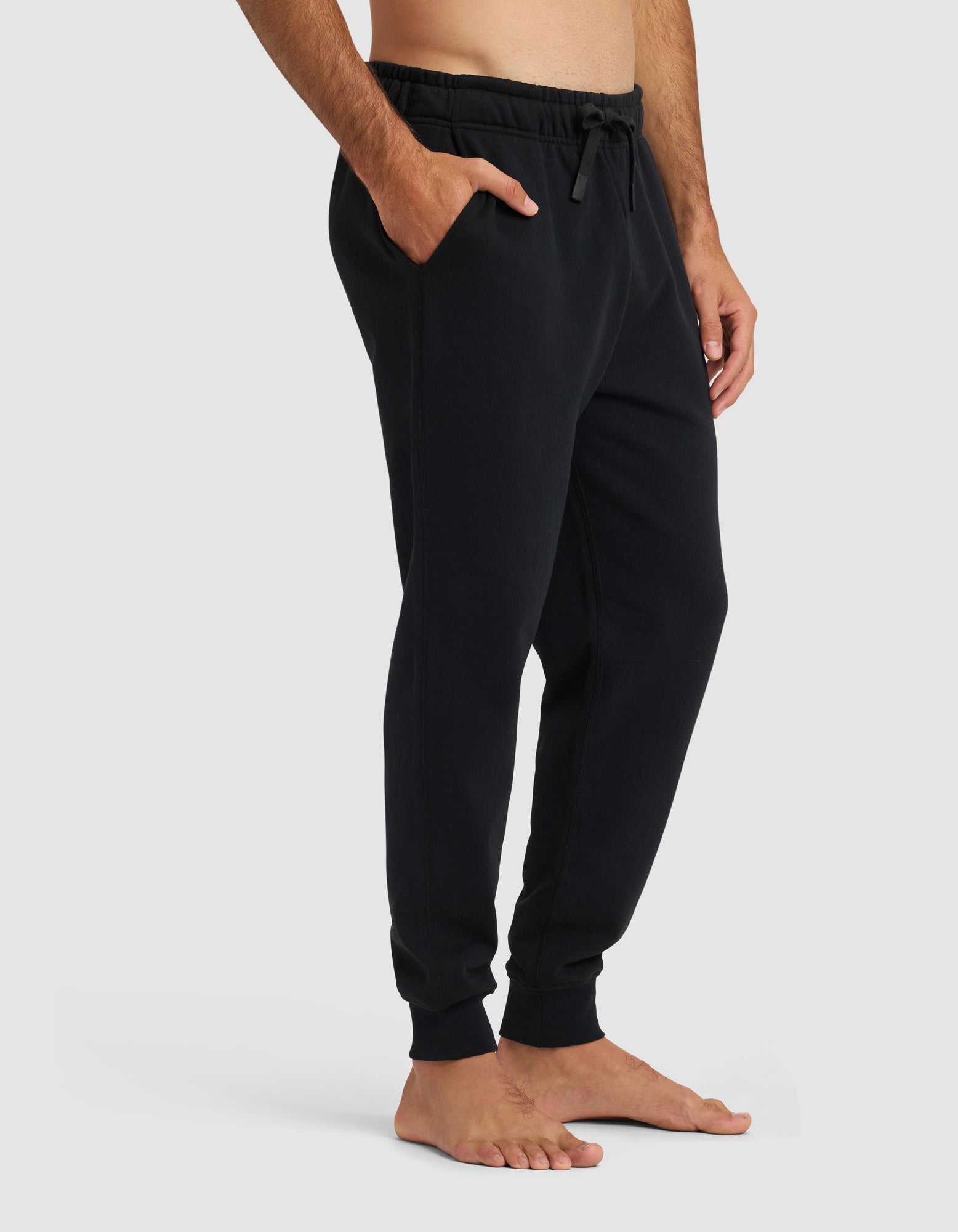 A barefoot person wears Cozy Earth's Men's Dylan Jogger, hands in pockets, against a plain light background. Only the lower torso and legs are shown.