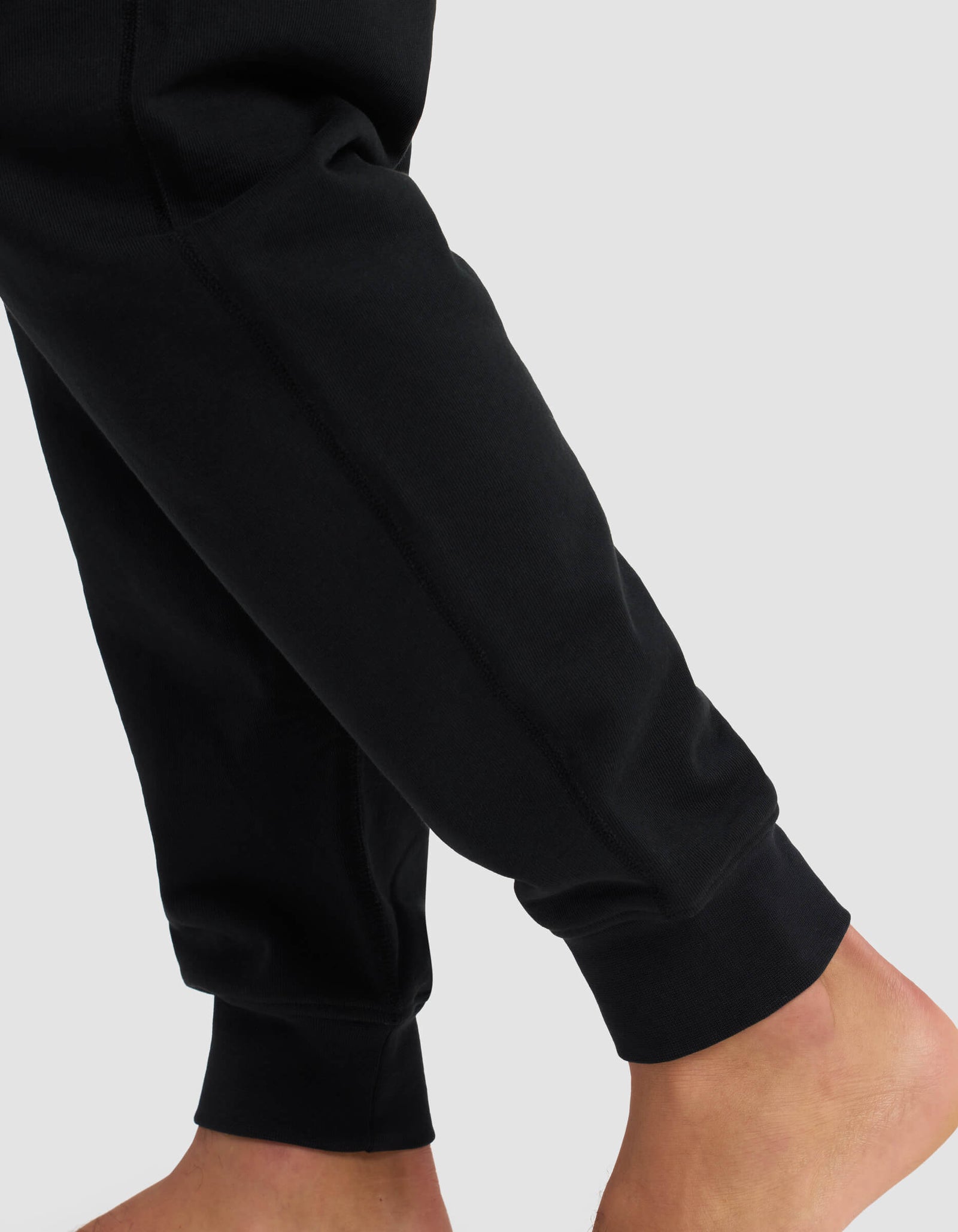 A close-up shows a person standing barefoot in Cozy Earth's Men's Dylan Jogger with ribbed cuffs, against a plain light gray background.