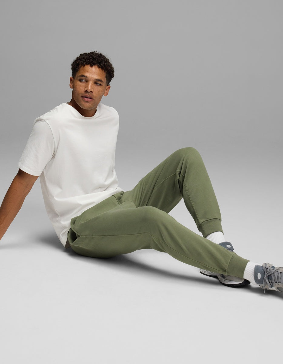 A man wearing a white t-shirt and olive green Men’s Dylan Jogger sits on the floor.