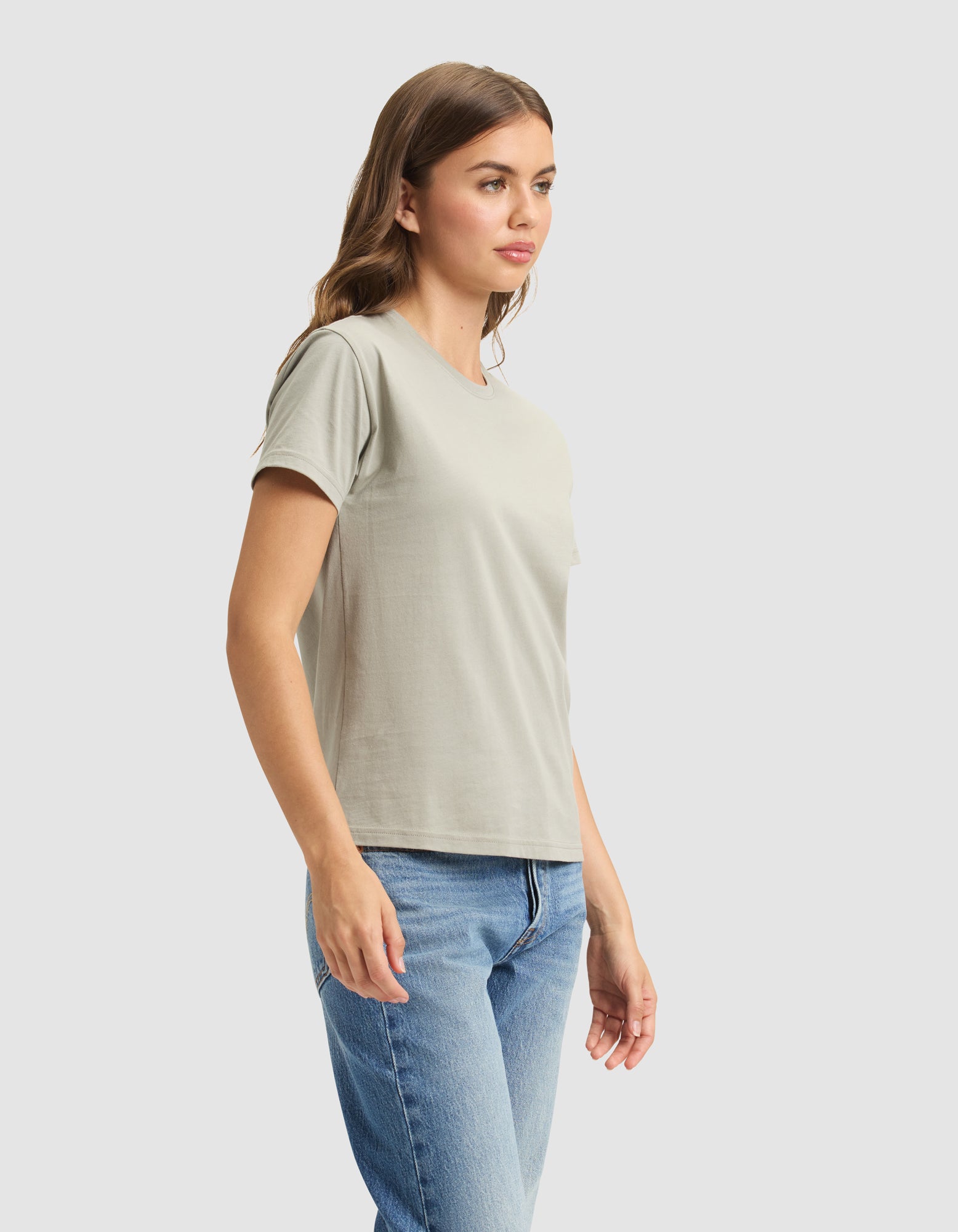A woman models the Cozy Earth Women's Easy Tee in light gray with blue jeans, standing slightly sideways against a plain light background. 