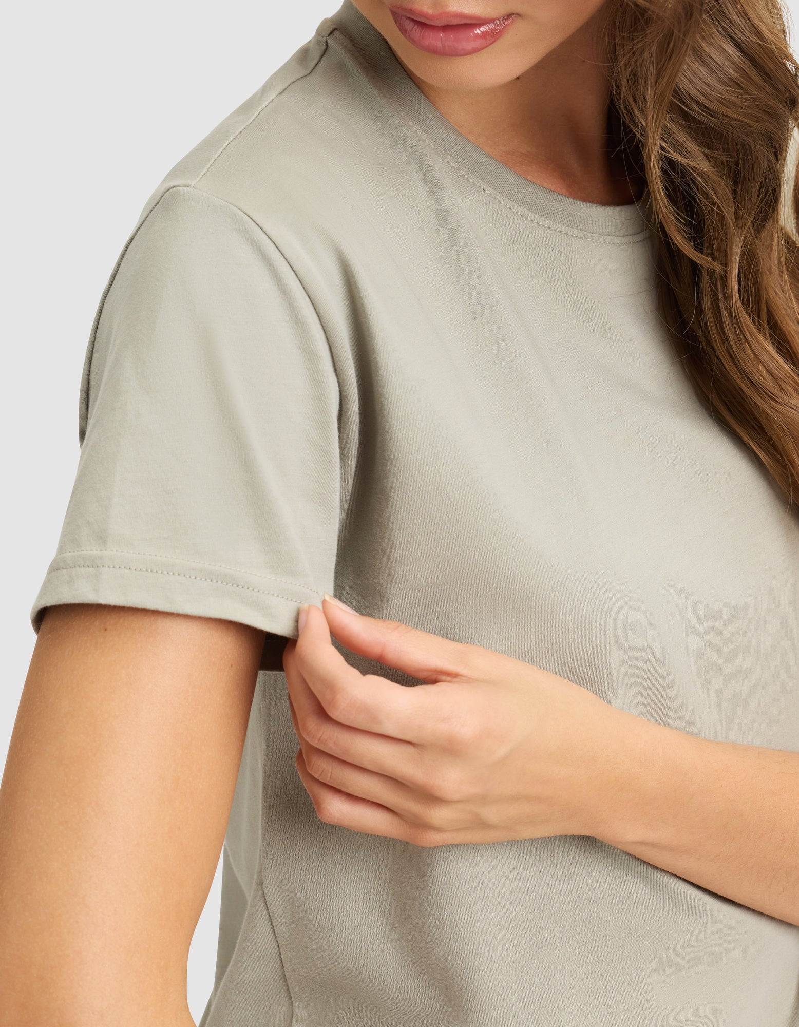 A woman wears the Cozy Earth Women's Easy Tee in light gray, gently holding her sleeve. Only the lower half of her face and upper body are visible. 
