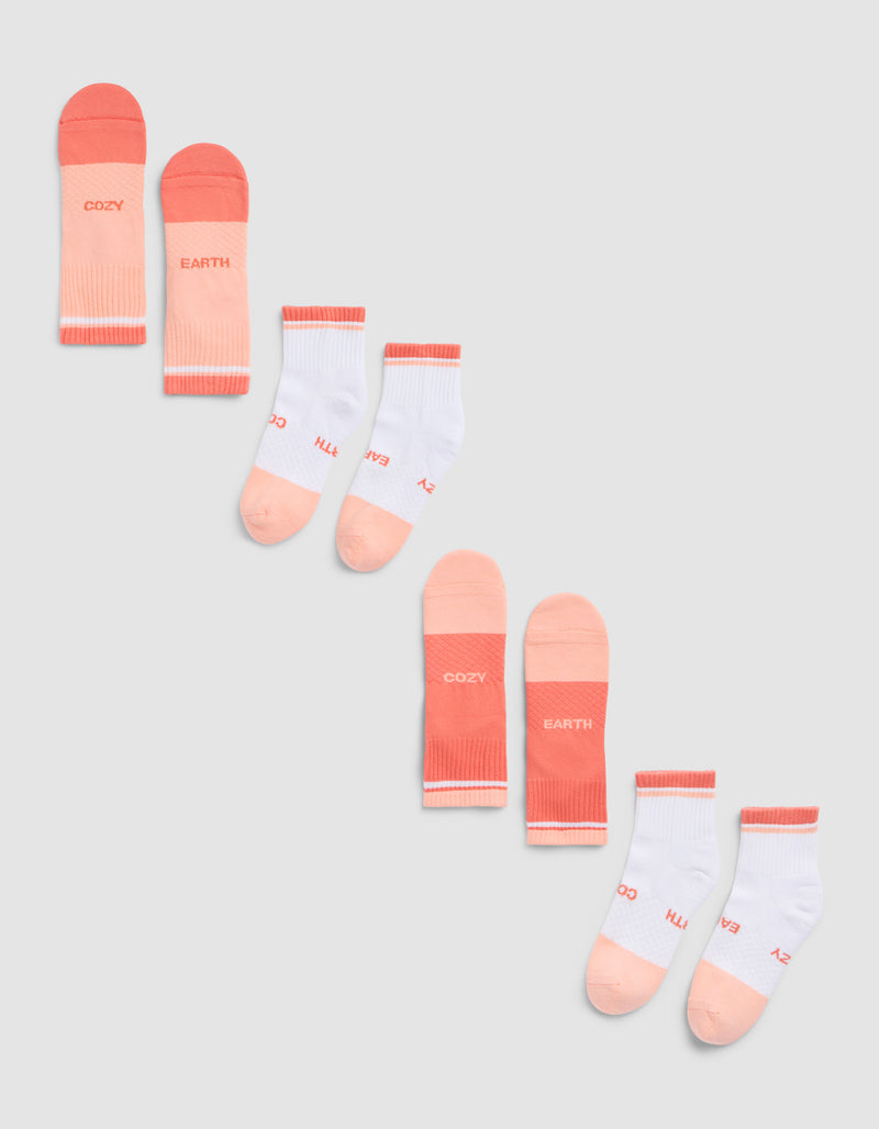 The Cozy Earth Essential Quarter Sock 4-Pack is shown on a gray background, featuring peach and pink pairs with "COZY" and "EARTH" text, plus white pairs accented in peach and pink with similar lettering.