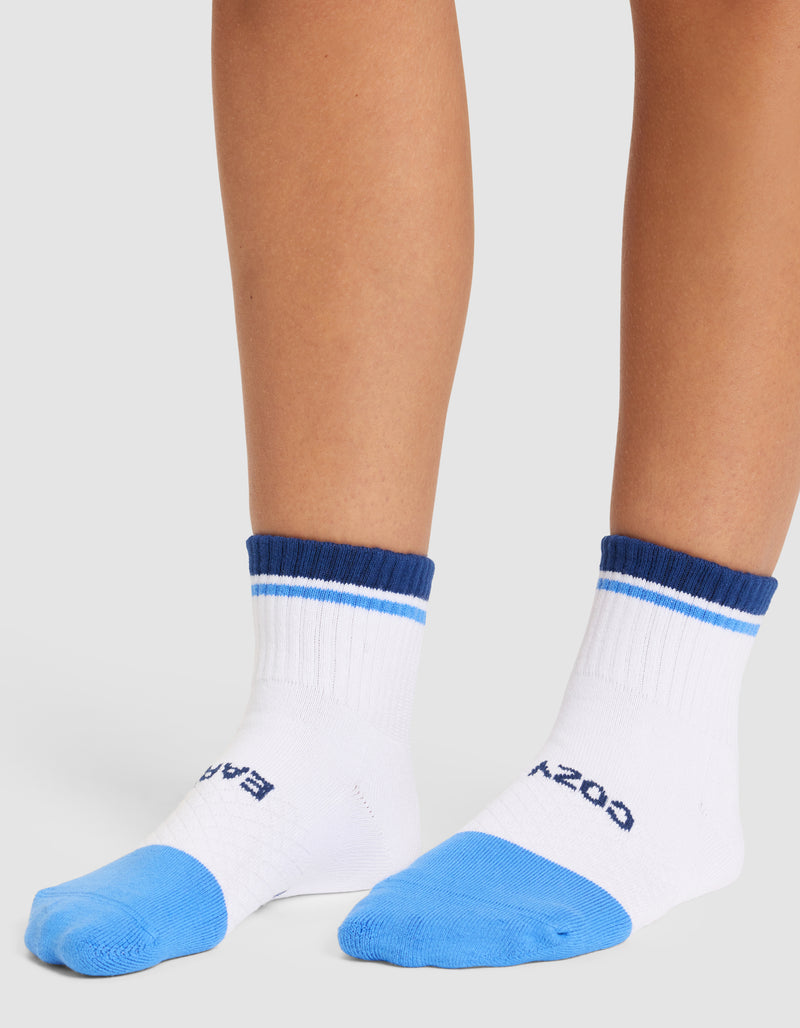 A person wears Cozy Earth Essential Quarter Socks in white with blue toes, cuffs, and stripes near the top. The socks feature text across the toes and are shown against a plain light background.