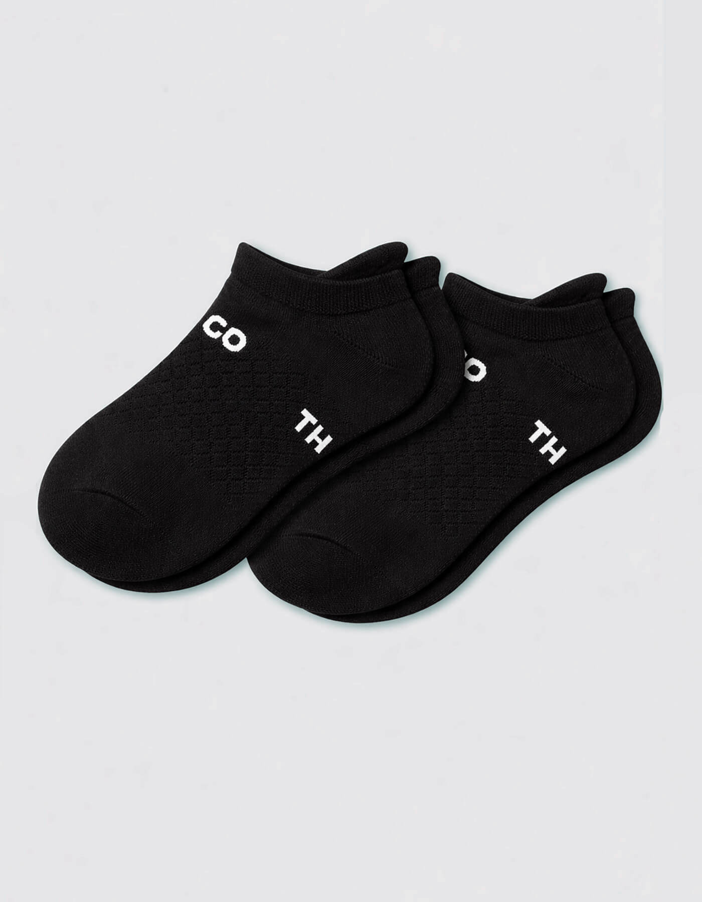 A pair of Women's Essential Ankle Socks by Cozy Earth in black, featuring white partial text "CO" and "TH" on top, displayed on a light gray background.|Color:Black