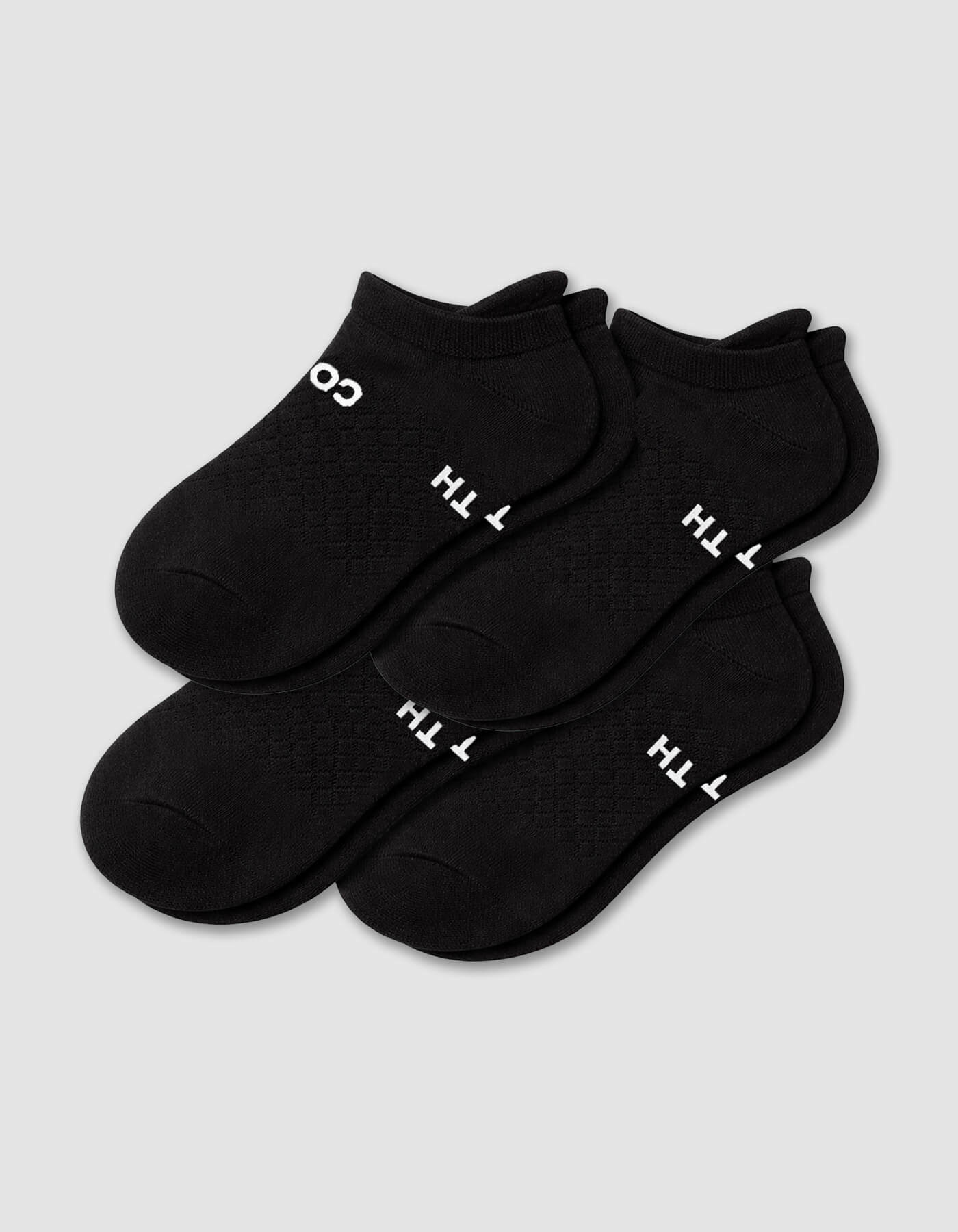 The Cozy Earth Men's Essential Ankle Sock 4-Pack in black features textured socks with partial white text on the soles, neatly stacked on a light gray background.