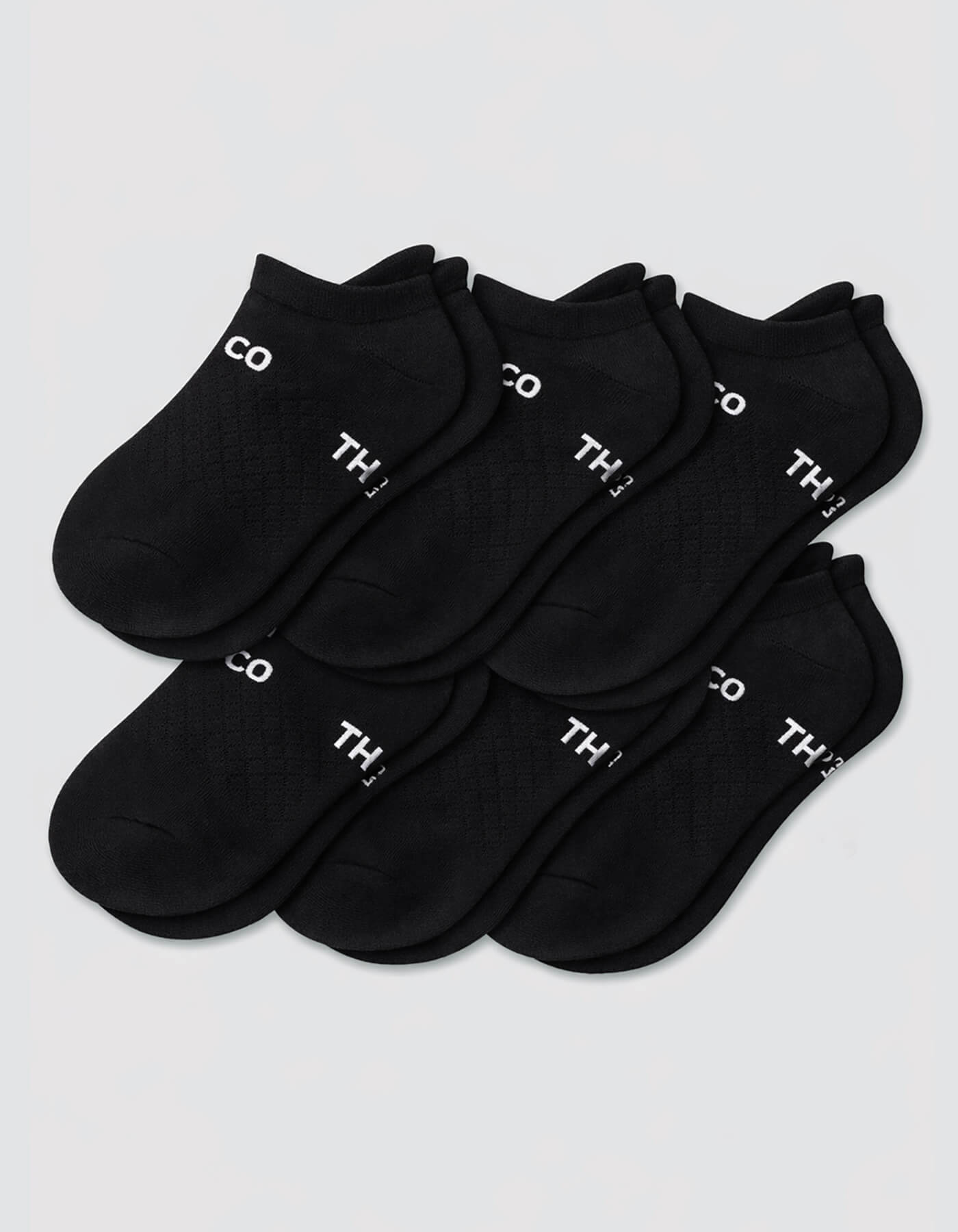 Six pairs of Cozy Earth Women's Essential Ankle Socks in black are arranged in two rows, each showing white "TH" text on the cuff, set against a plain light gray background.|Color:Black