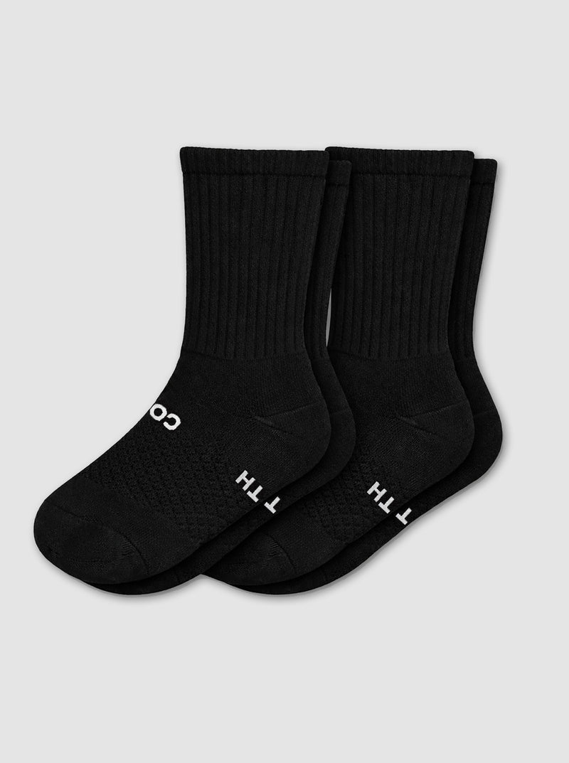 Two pairs of Cozy Earth Women's Essential Calf Socks in black, featuring ribbed cuffs and small white lettering on the soles, are laid side by side on a light gray background.