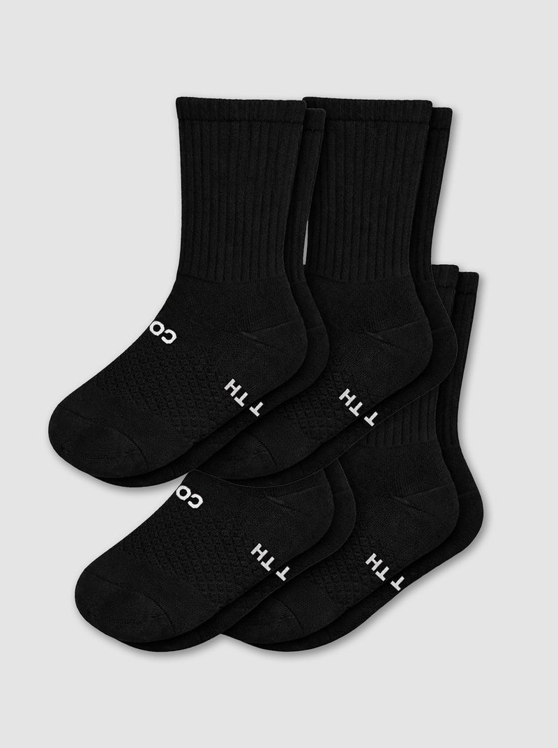 The Cozy Earth Women's Essential Calf Sock 4-Pack in black, featuring ribbed cuffs and white text near the toes, is arranged overlapping on a light gray background.