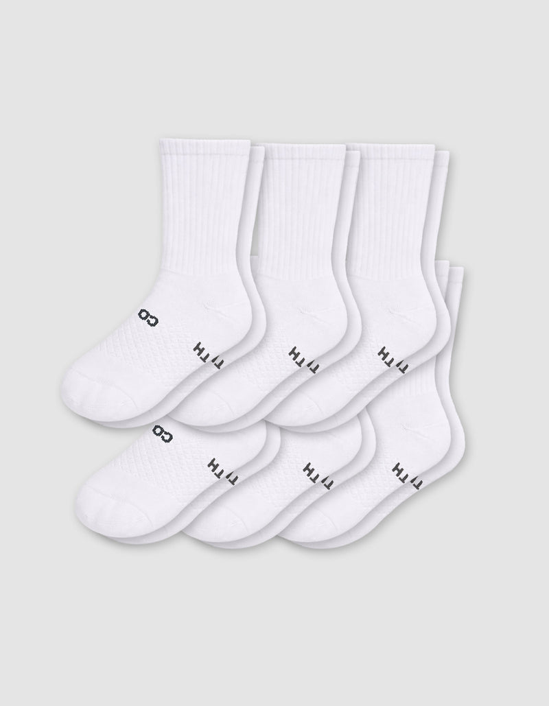 Six pairs of Cozy Earth Men's Essential Calf Socks in white are arranged in two rows on a light gray background, each featuring small black text and a symbol near the toes and ribbed cuffs.