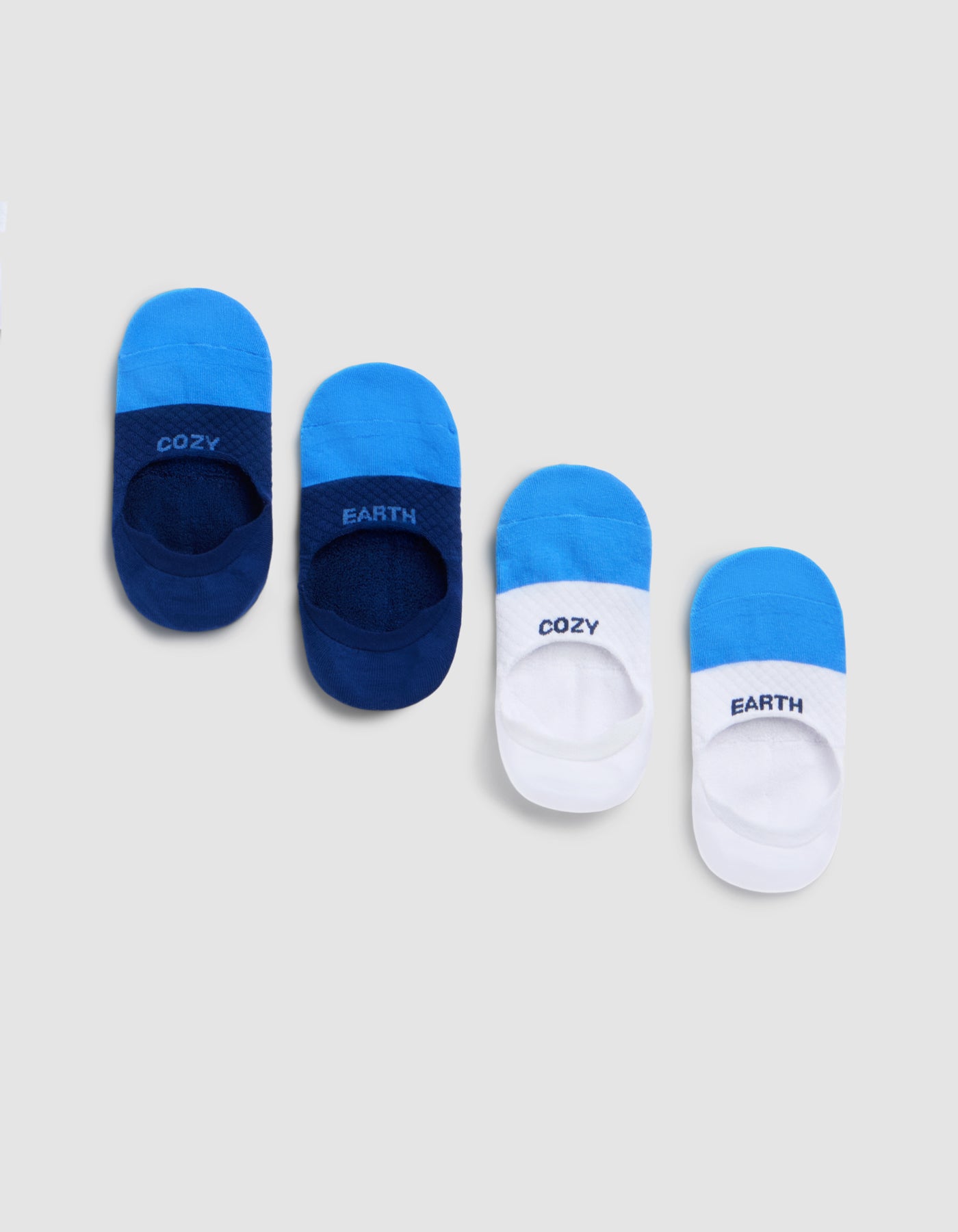 Four pairs of Cozy Earth Essential No-Show Socks in blue and white are arranged diagonally on a gray background. Two pairs are mainly dark blue with "COZY" and "EARTH," while the other two are mostly white with the same text. 
