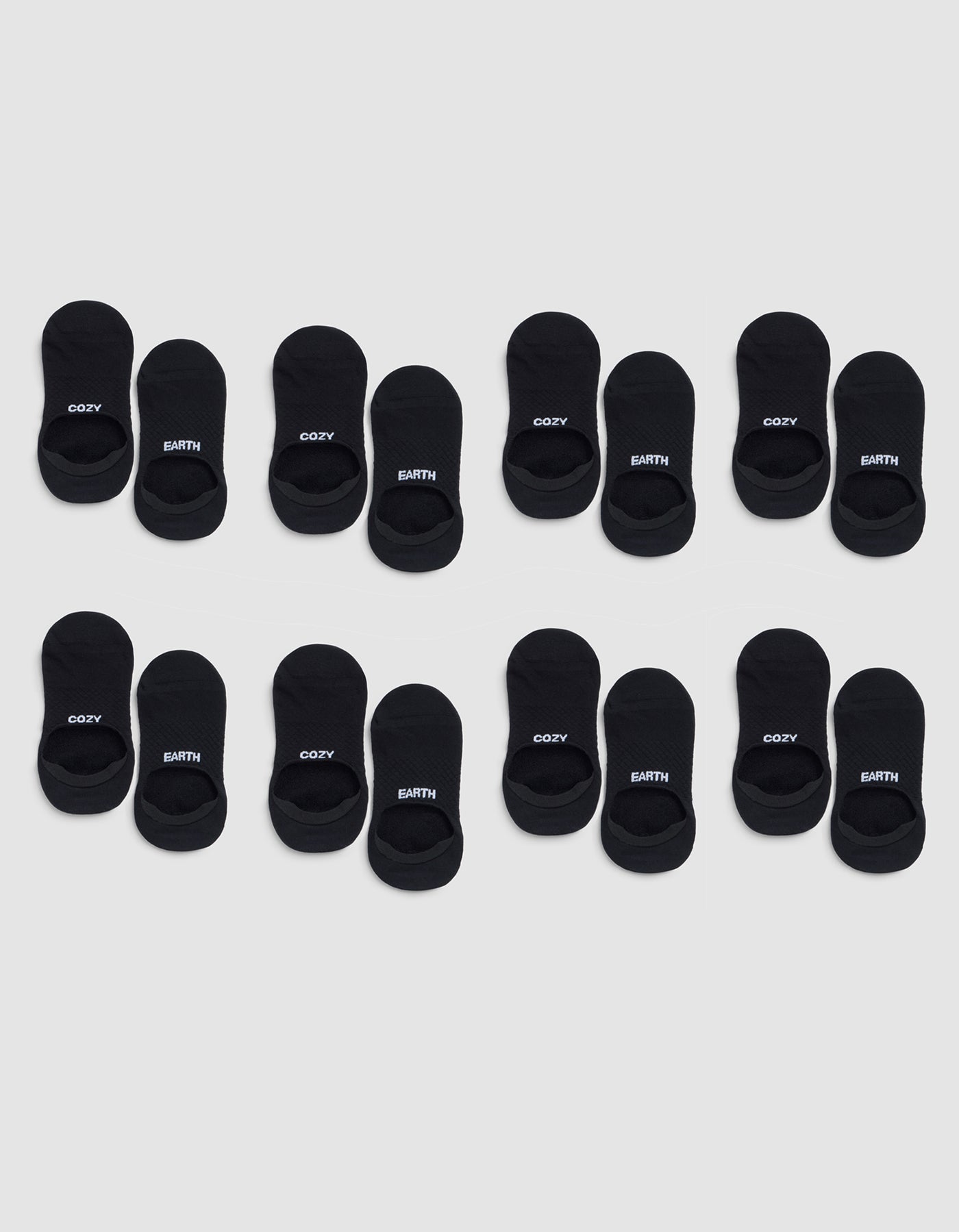 Eight pairs of Cozy Earth Essential No-Show Socks are arranged in three rows on a light gray background, with "COZY" and "EARTH" printed in white letters on the black socks. 