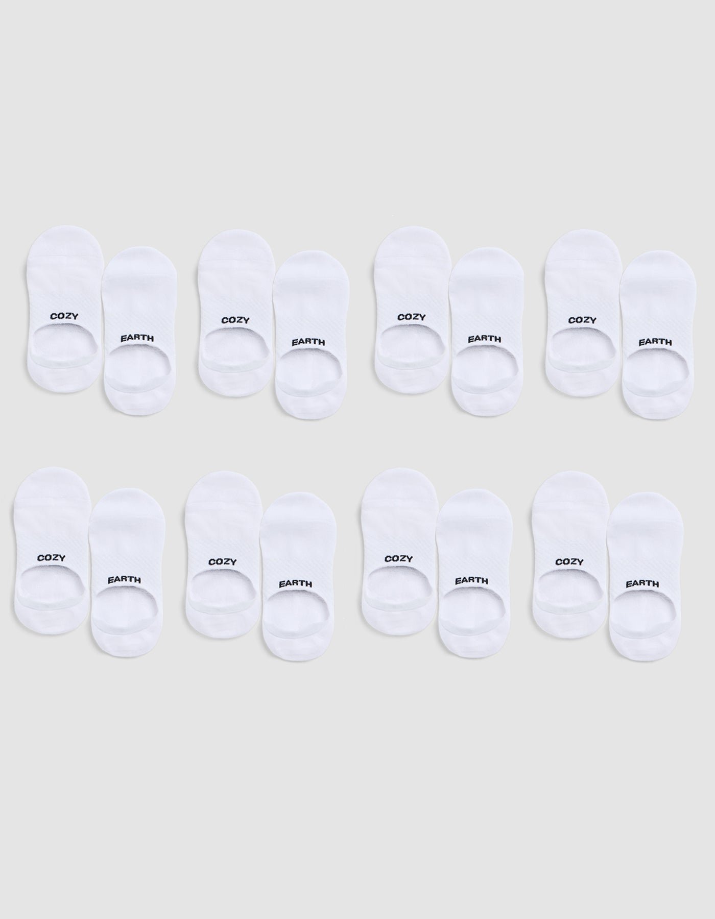 Eight pairs of white Essential No-Show Socks by Cozy Earth are arranged in three rows on a light gray background; each pair is labeled “COZY” on one sock and “EARTH” on the other. |Color:White