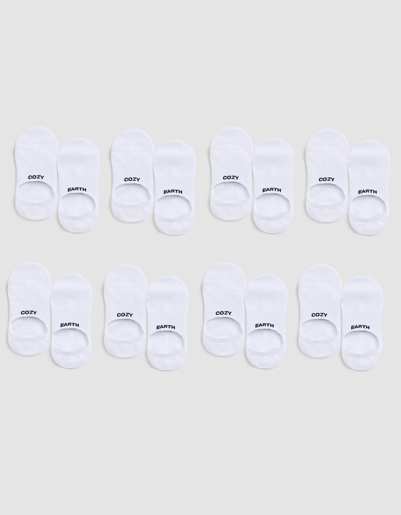 Eight pairs of white Essential No-Show Socks by Cozy Earth are arranged in three rows on a light gray background; each pair is labeled “COZY” on one sock and “EARTH” on the other. 