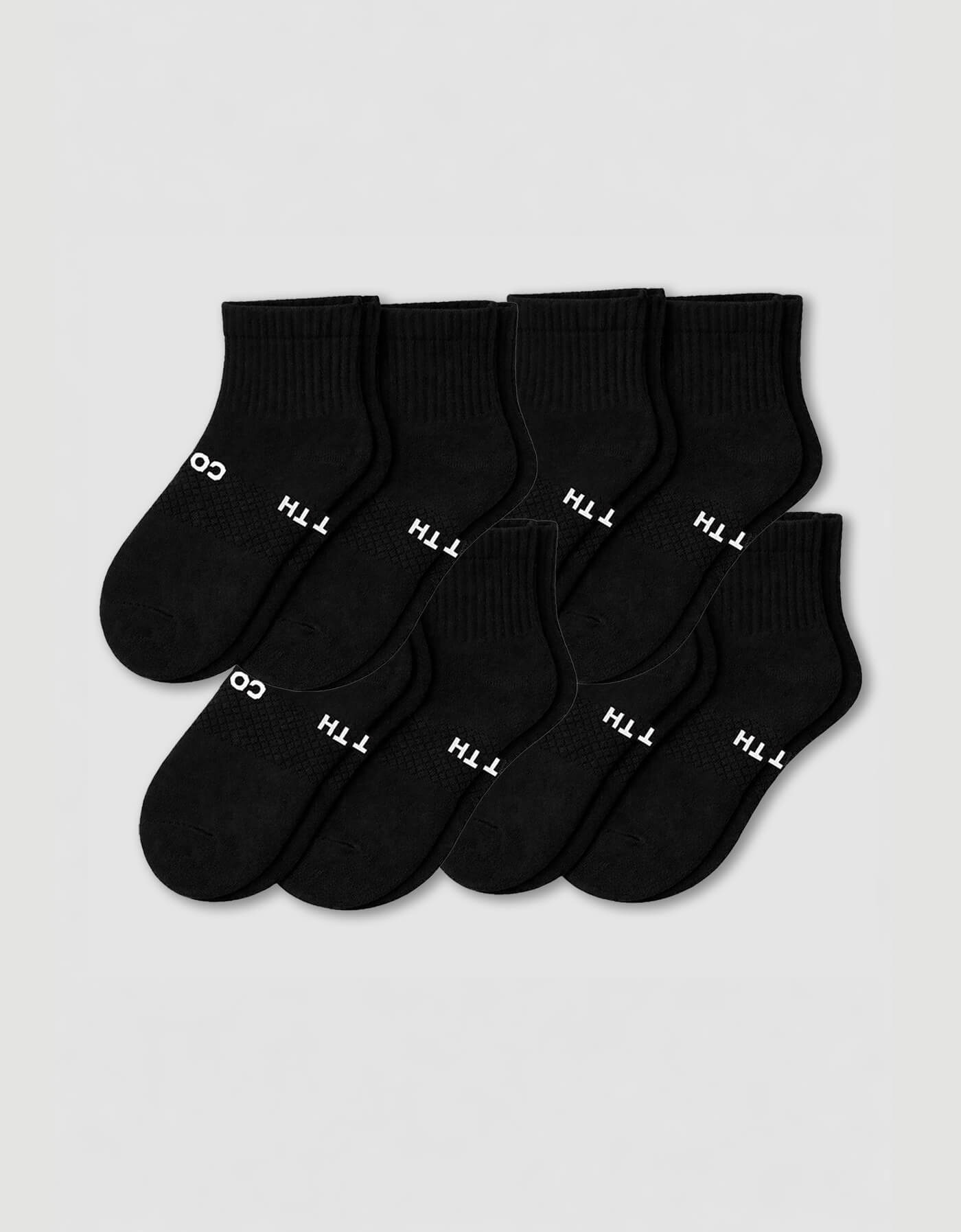 The Cozy Earth Men's Essential Quarter Sock 8-Pack features eight pairs of black socks with ribbed cuffs, neatly arranged in overlapping rows. Some have white text near the toe area, all displayed on a plain light background.