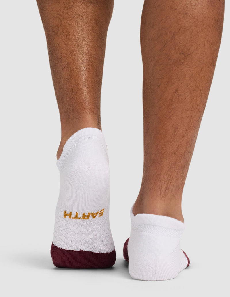 A person wearing Cozy Earth Essential Ankle Socks in white with maroon soles and "EARTH" in yellow on the left heel; the back of their lower legs is shown against a plain background.
