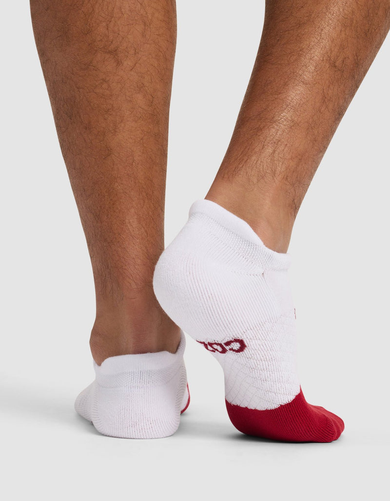 A person models the Cozy Earth Essential Ankle Sock in white with red toes, standing on a light background and displaying the back and side views of their lower legs and feet.