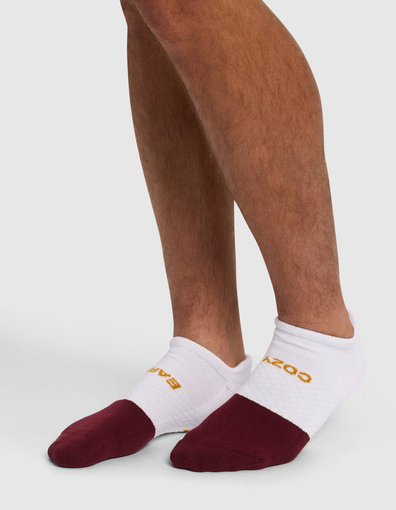 A person wearing Cozy Earth Essential Ankle Socks with maroon toes and yellow text stands on a light surface, showing only their lower legs and feet.