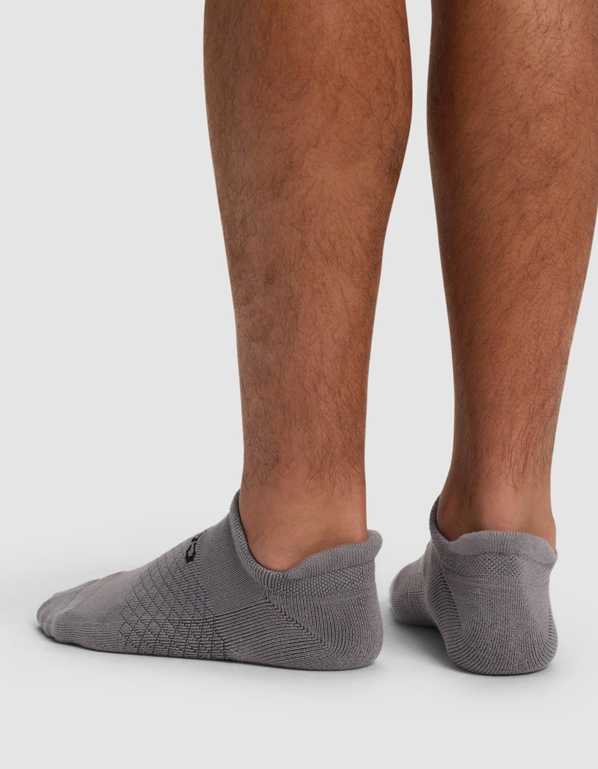 Back view of a person wearing Cozy Earth Essential Ankle Socks, low-cut gray socks that barely cover the ankles, standing on a white surface with lower legs visible.