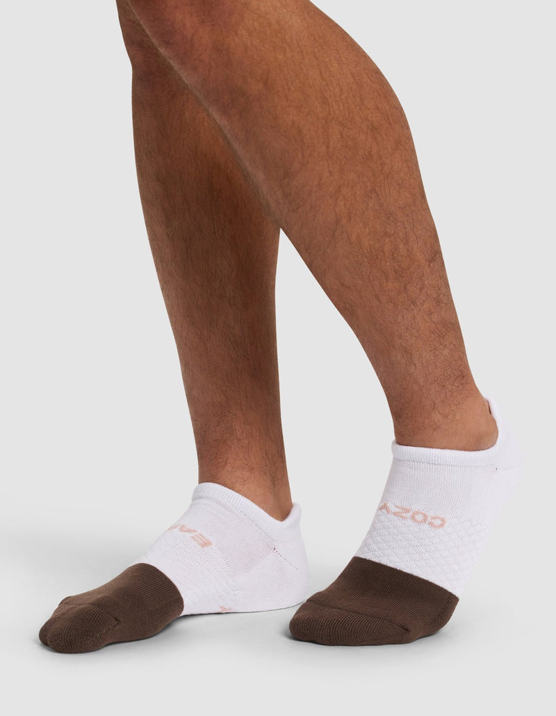 A person wears Cozy Earth Essential Ankle Socks with brown toes, standing on a light grey surface. Only the feet and lower legs are shown.