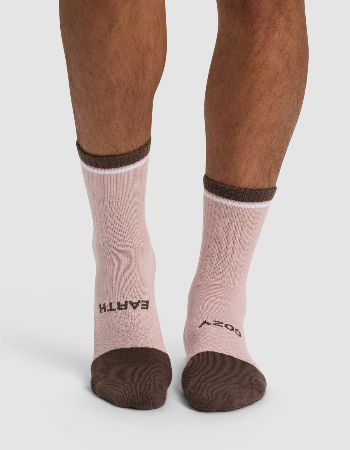 A person wears Cozy Earth's Essential Calf Socks in pink with brown toes and cuffs; "EARTH" is printed in black on the left sock and "BODY" on the right, both across the tops of the feet.