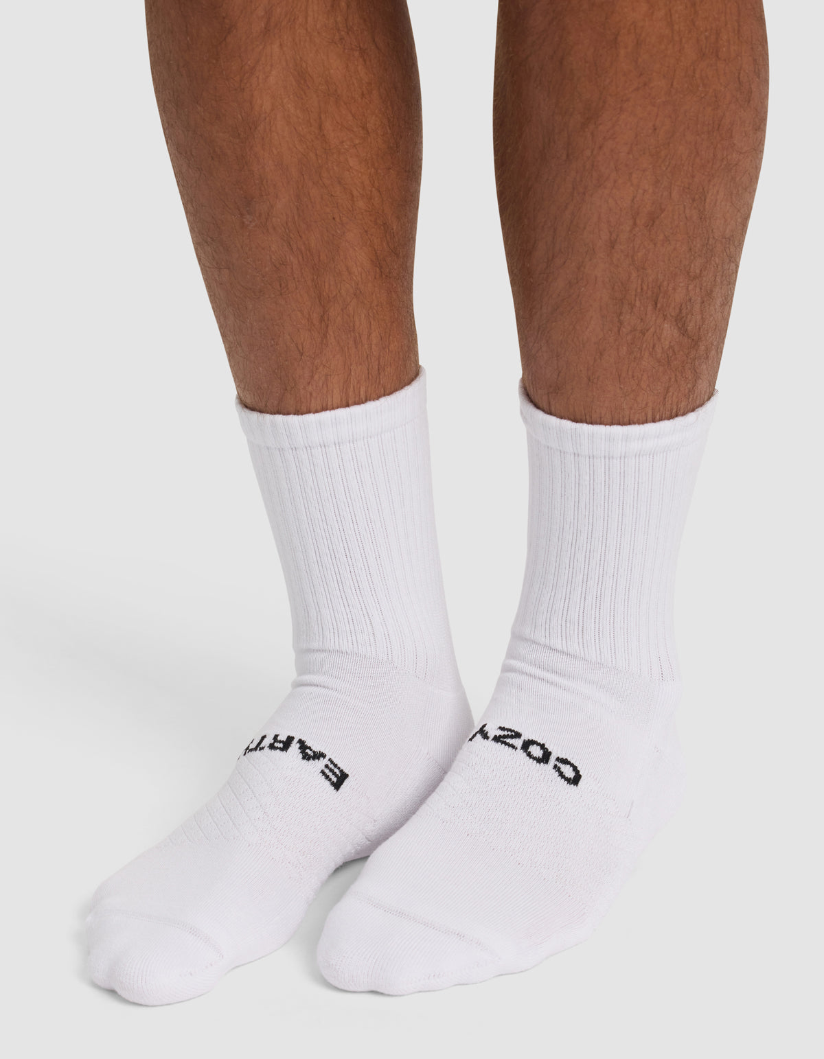 A person wearing Cozy Earth Essential Calf Socks with black text near the toes stands on a white surface. Only their lower legs and feet are visible.