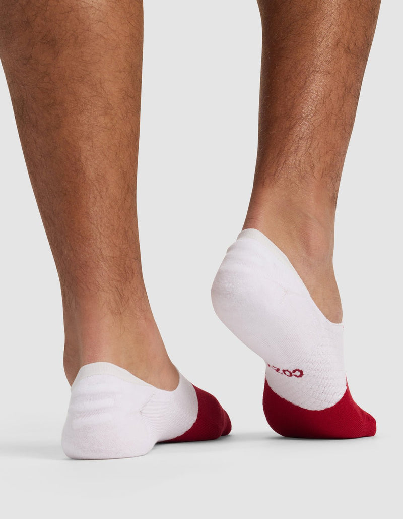 A person stands on tiptoe, highlighting the Cozy Earth Essential No-Show Sock in white with red toes. The plain, light background emphasizes the socks and lower legs.