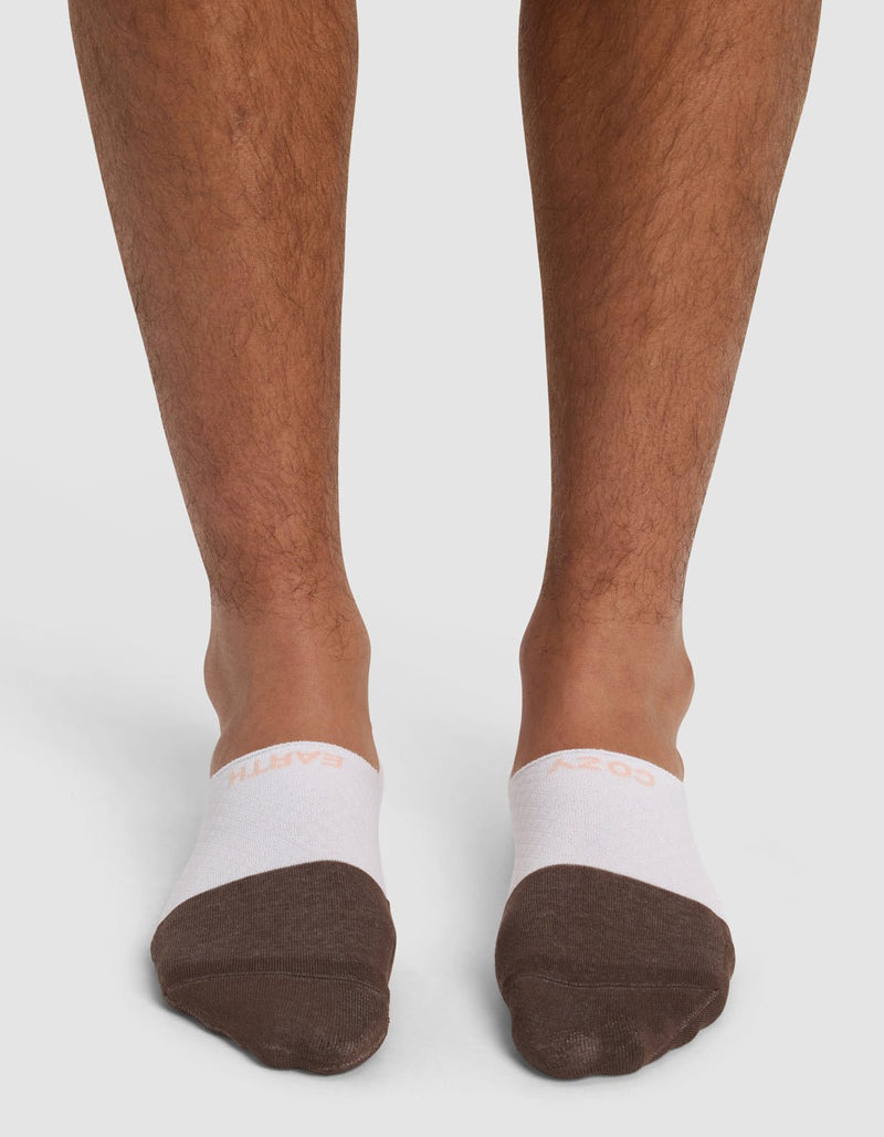 Close-up of a person's lower legs and feet wearing Cozy Earth's Essential No-Show Sock in white and brown, standing on a plain white background.