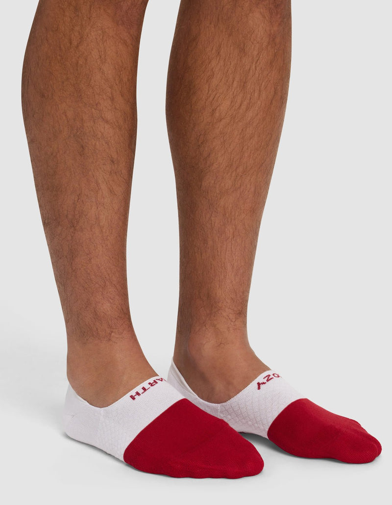A person wearing Cozy Earth's Essential No-Show Sock in white and red, which covers only the foot and not the ankle, standing on a white background.