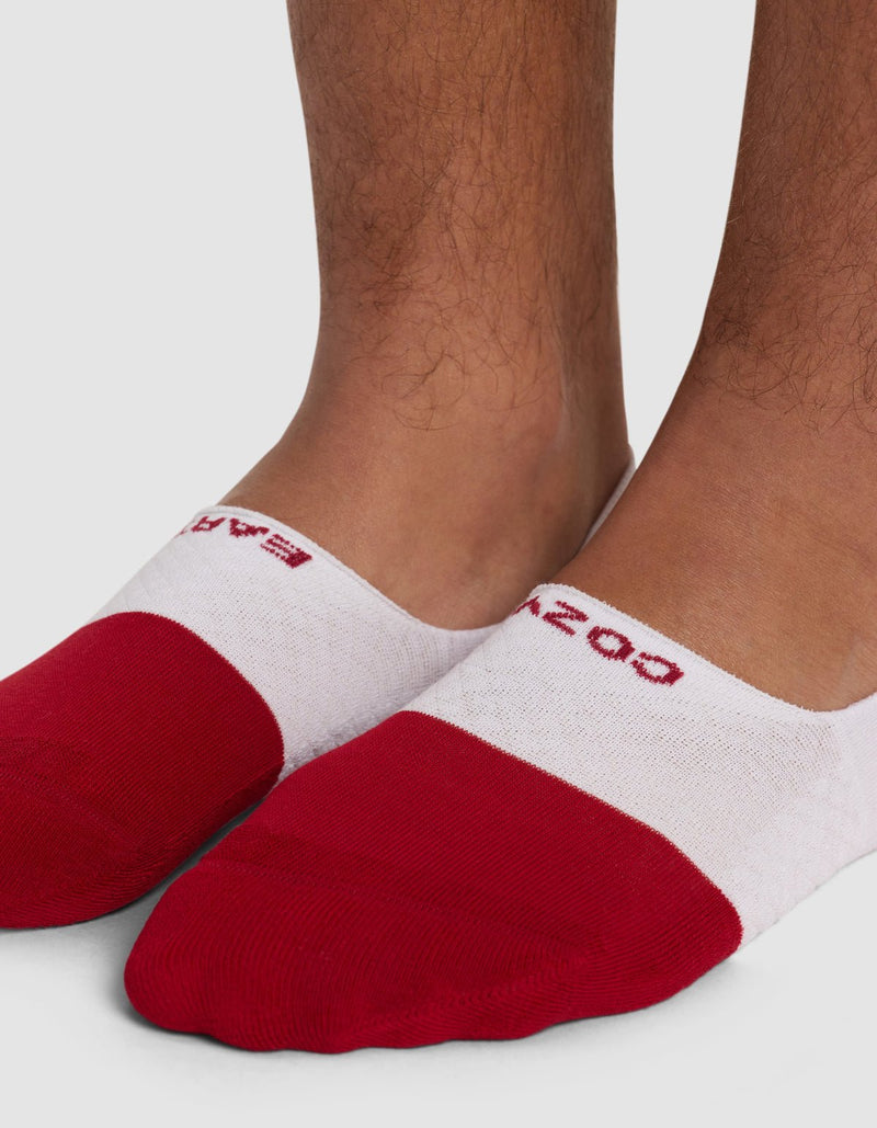 A close-up of feet wearing Cozy Earth Essential No-Show Socks, featuring red toes, white middles, and red lettering on top, shown against a plain background.