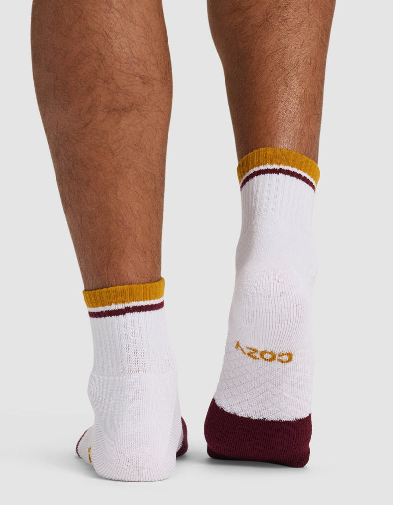 A close-up of the back of lower legs wearing Cozy Earth Essential Quarter Socks—white ankle socks with maroon and gold striped cuffs, maroon heels, and "COZY" in gold lettering on one sole.