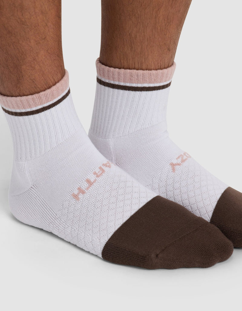 A close-up of feet wearing Cozy Earth's Essential Quarter Socks in white, featuring brown toes and rims with light pink trim near the cuffs. The brand name appears subtly on the sides.