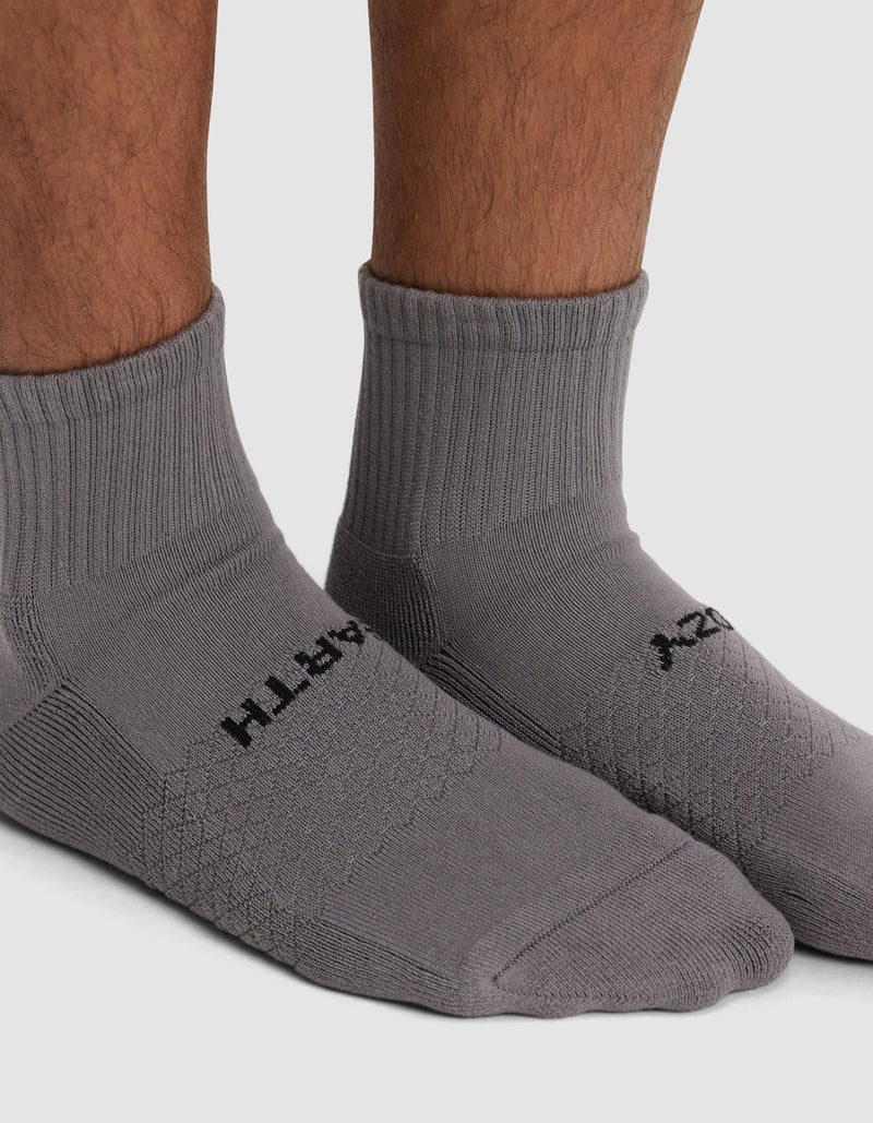 Close-up of a person wearing Cozy Earth's Essential Quarter Sock in gray with black text, standing on a white background.