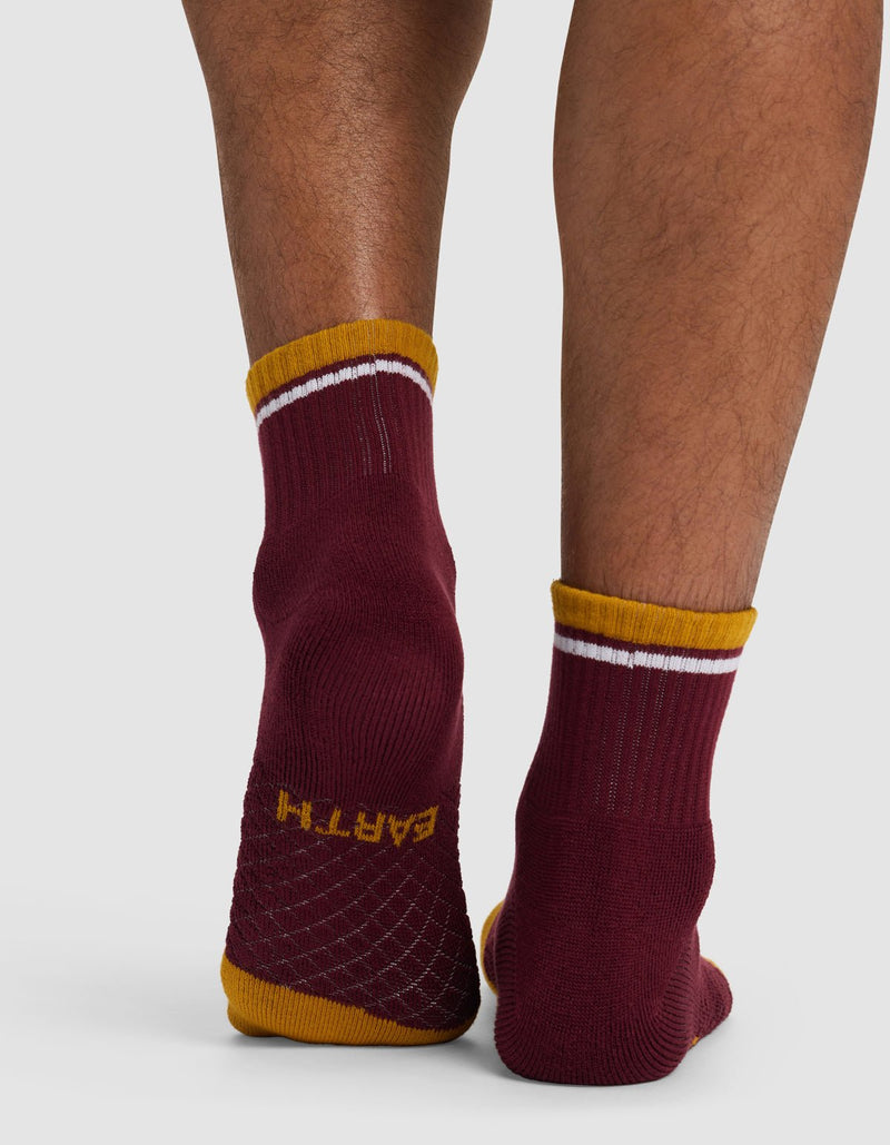 Someone stands on tiptoe wearing Cozy Earth Essential Quarter Socks in maroon with yellow and white trim. The textured grip soles display the word "EARTH" in yellow on one sock.