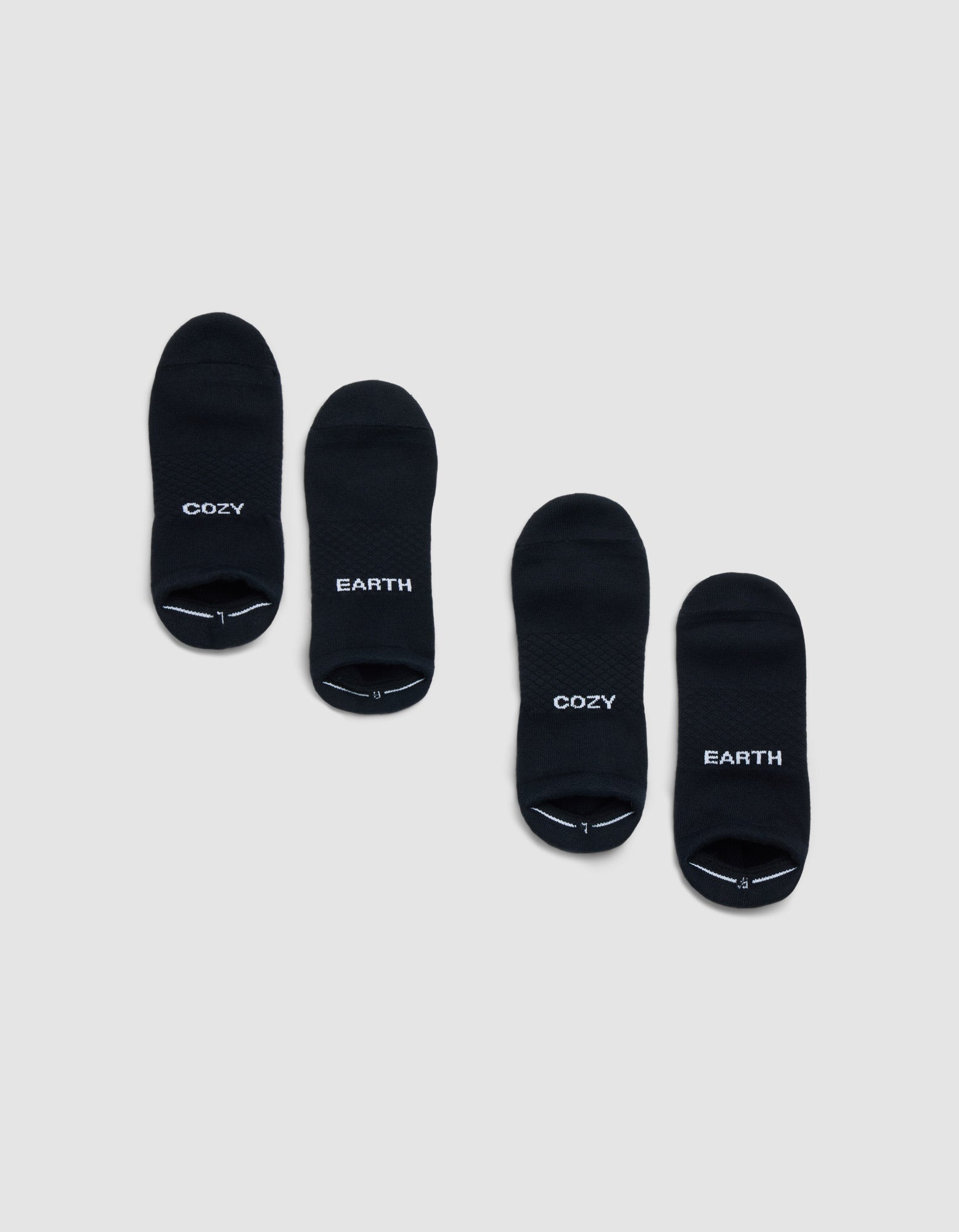 Two pairs of Cozy Earth Essential Ankle Socks in black are shown on a light gray background; each pair features "COZY" and "EARTH" in white lettering, both with matching style. 