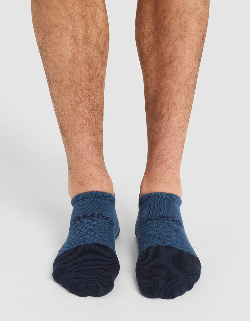 A pair of feet wear Cozy Earth's Essential Ankle Sock in blue with dark blue toes and heels, shown from the front on a plain white background.