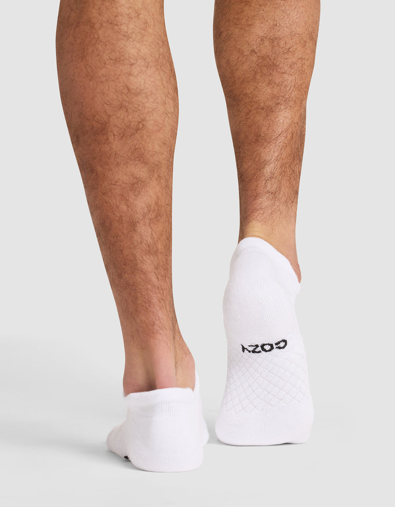 Back view of a person wearing Cozy Earth Essential Ankle Socks in white, which cover the feet up to the ankles. "COZY" is printed in black on the sole. The background is plain and light-colored.