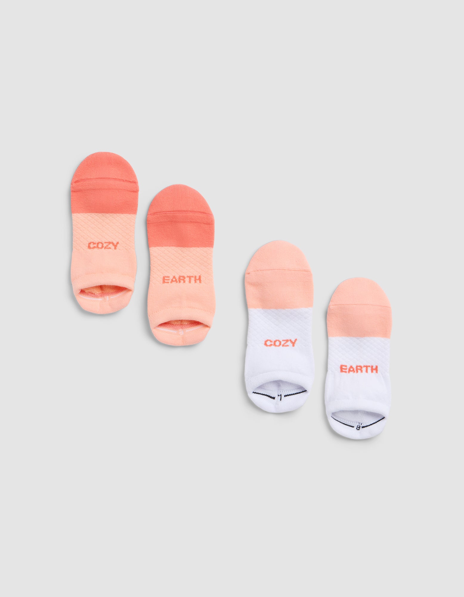 Four Essential Ankle Socks by Cozy Earth, in peach and white gradients, are paired on a light gray background. Each pair shows "COZY EARTH" or "EARTH"/"COZY" in soft gradient lettering. 